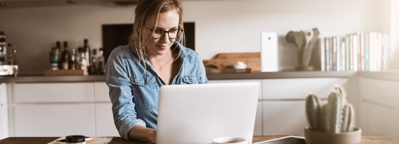 An image of a woman sitting in a kitchen working on a laptop.