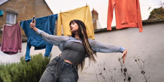 a girl holding a phone dancing in the garden.